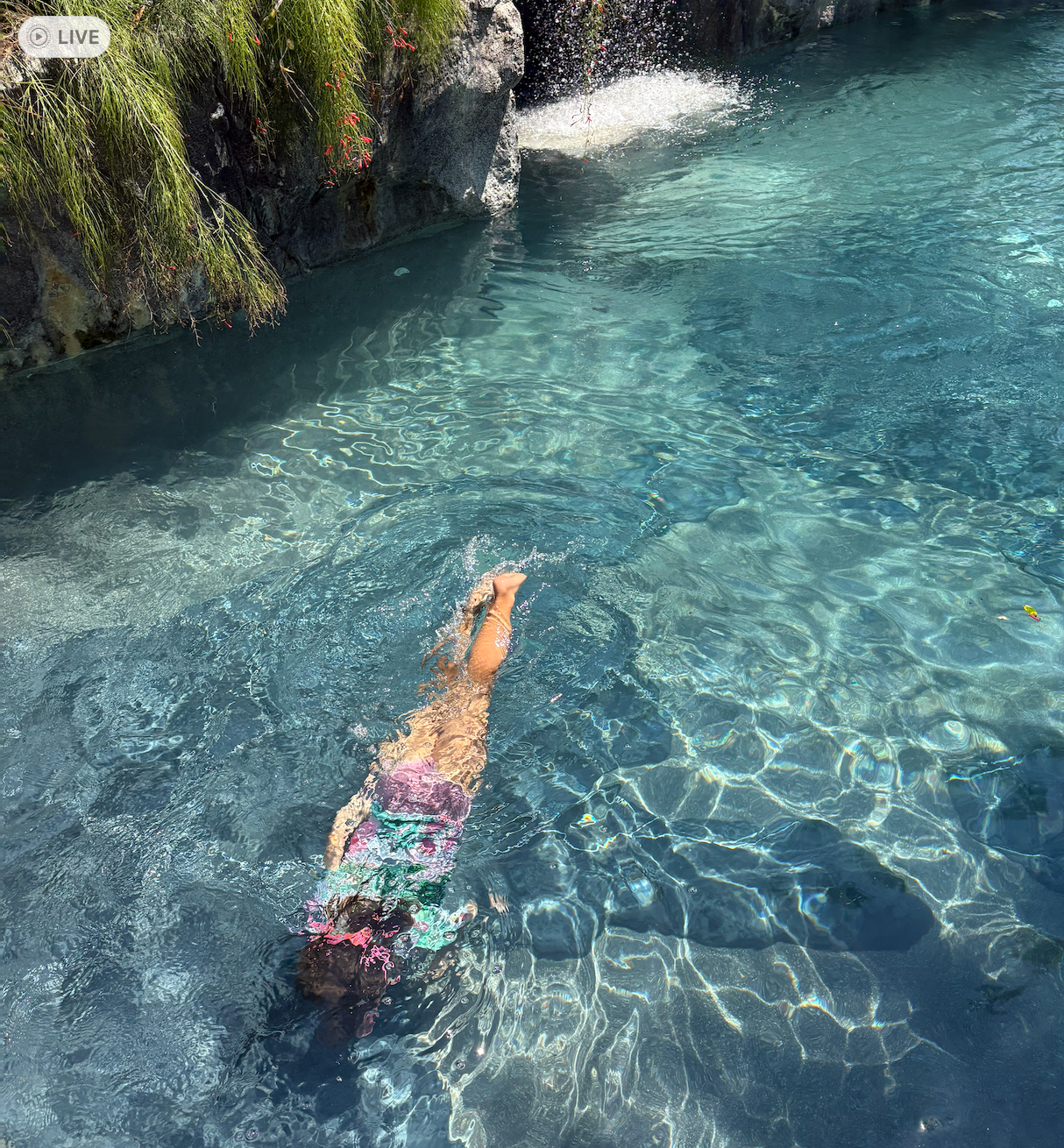 A child swimming in a clear natural rock pool fed by a small cascade