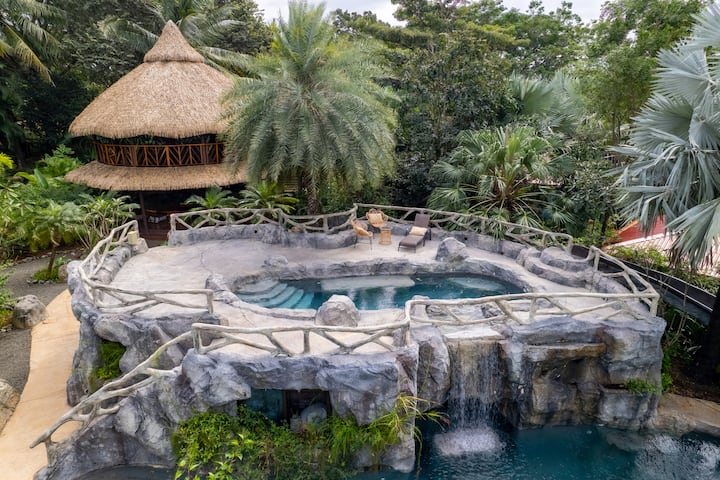 The thatched casita beside the hotel's natural rock-cut cave pool and waterfall, framed by jungle